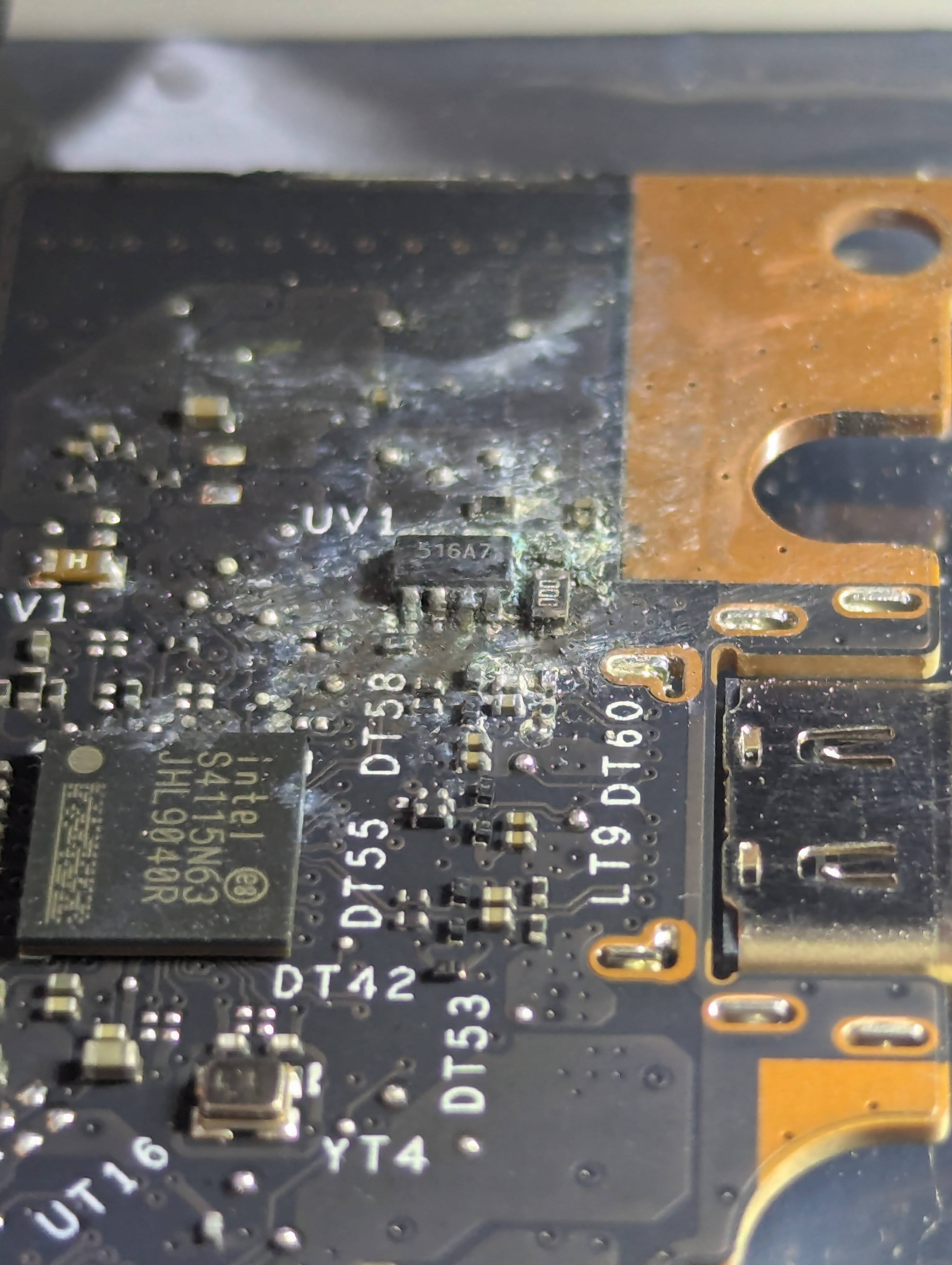 A close up of a laptop motherboard showing a 6 pin power management chip completely corroded and covered in gunk